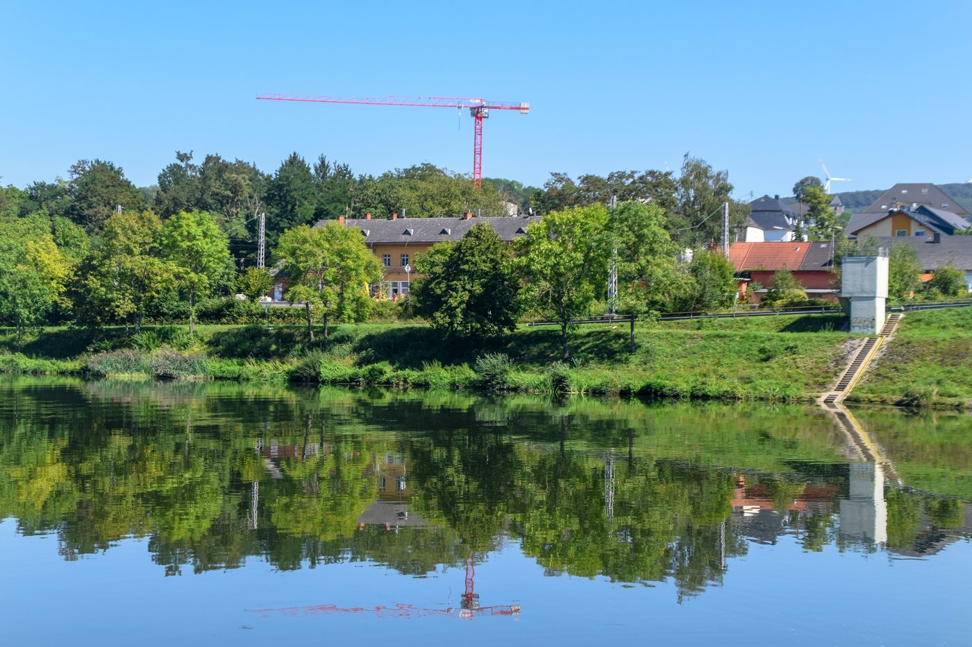 Bewachsenes Moselufer mit Häusern und Spiegelung im Wasser