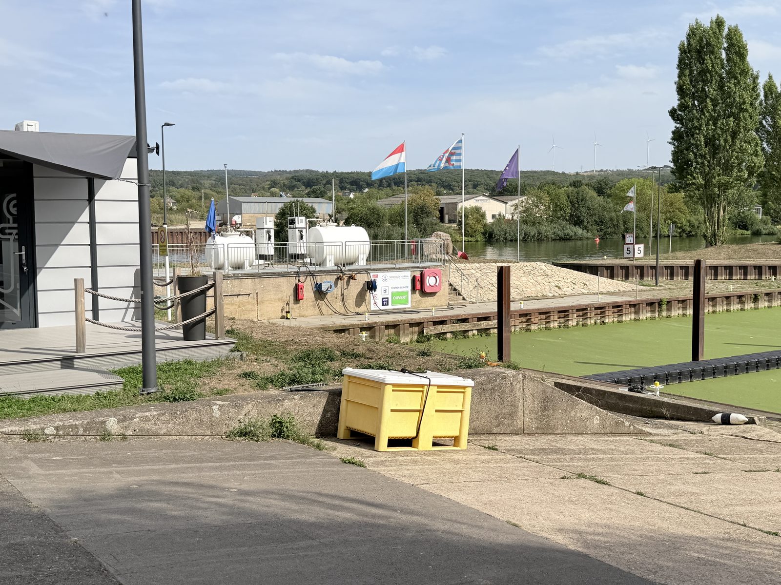 Bootstankstelle mit zwei Zapfsäulen und Tanks am Ufer, dahinter Flaggen
